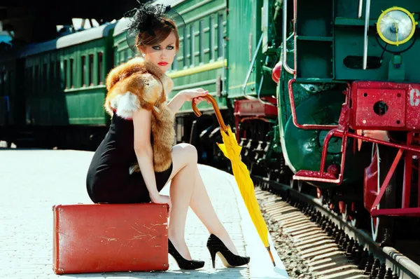Chica retro sentada en la maleta en la estación de tren — Foto de Stock