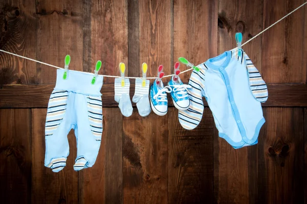 Asciugatura vestiti per bambini sulla clothesline, sfondo di tavole marroni . — Foto Stock