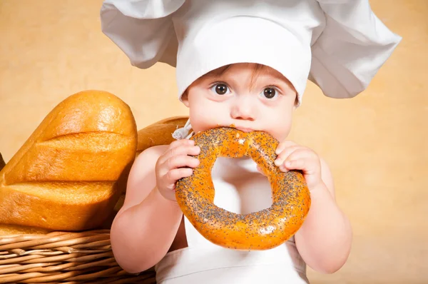 Pequena cozinheira com um bagel nas mãos . — Fotografia de Stock