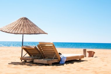 kumlu sahil üzerinde rattan ve şezlong şemsiye.