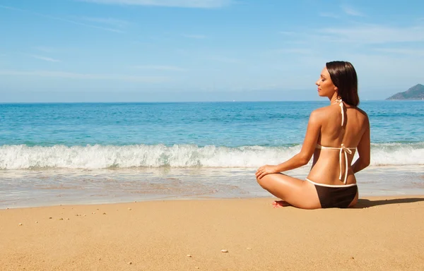 Brunette sitting on the beach in a lotus position — Stock Photo, Image