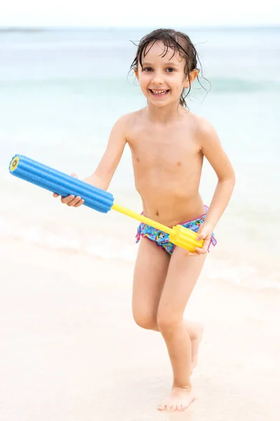 Śmiesznie uśmiechnięta dziewczynka biegnie do morza wzdłuż piaszczystego brzegu z rozbryzgiem w rękach. Wakacje letnie i gry na plaży — Zdjęcie stockowe