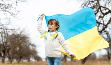 Sarı ve mavi kurdeleli küçük bir kız ve rüzgarda dalgalanan Ukrayna bayrağı. Ukrayna 'daki savaşı durdurun. Yüksek kalite fotoğraf