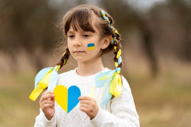 Küçük bir kız göğsünün yanında Ukrayna bayrağının vatansever renginde sarı ve mavi bir kalp tutuyor. Ukrayna 'daki savaşı durdurun. Ukrayna ulusunu kurtarmaya yardım et. Yüksek kalite fotoğraf