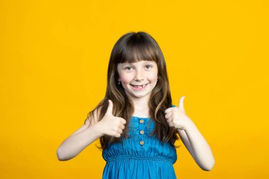 Gülümseyen küçük bir kız parmağını kaldırdı ve Cool 'u gösterdi, Süper. Ağızda süt dişleri kaybolmuş. Dişçi konsepti. Sarı arka planda izole edilmiş. Yüksek kalite fotoğraf
