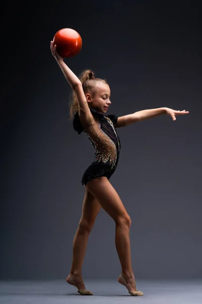 A little gymnast in a performance costume does acrobatic exercises with a ball. The girl wants to win. High quality photo