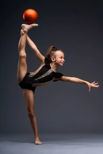A little gymnast in a performance costume does acrobatic exercises with a ball. The girl wants to win. High quality photo