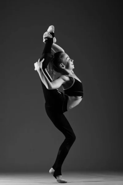 穿着运动服的年轻而灵活的女子体操运动员做体操伸展运动 她把腿放在头上 白色背景上的黑白照片 高质量的照片 — 图库照片