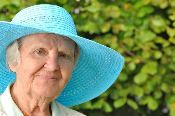 Starší žena v modrém klobouku venku v zahradě. — Stock fotografie
