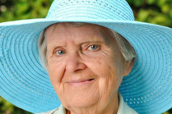 Senior vrouw in blauwe hoed buiten in de tuin. — Stockfoto