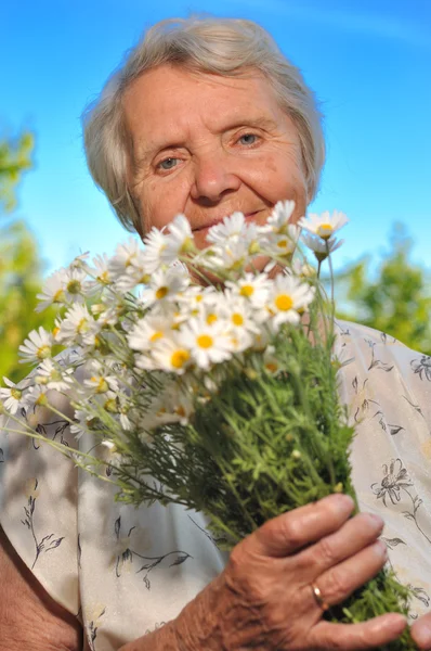 Seniorin riecht Blumen am blauen Himmel. — Stockfoto