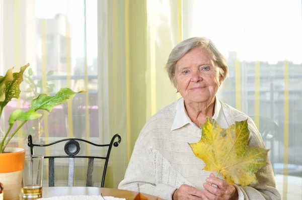Senior woman with autumn leaf in home. — Stock Photo, Image
