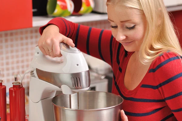 Junge blonde Frau mit einem Mixer in roter Küche. — Stockfoto