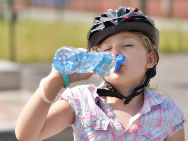 Ung flicka i en cykel hjälm dricksvatten. — Stockfoto