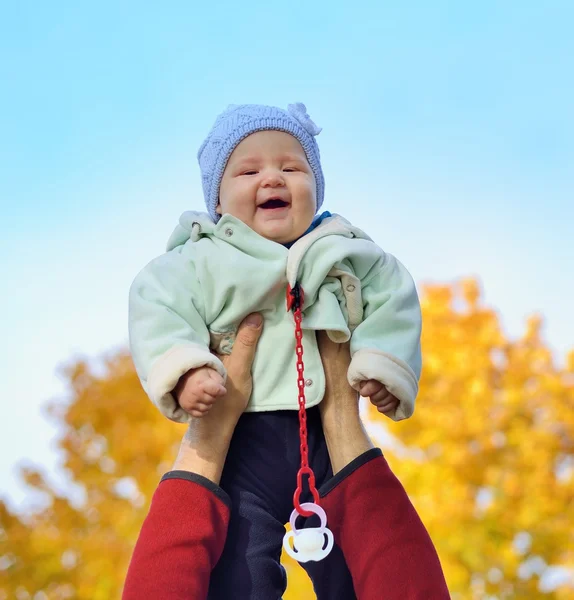 Happy smiling baby held up by his father against the sky. Stock Image