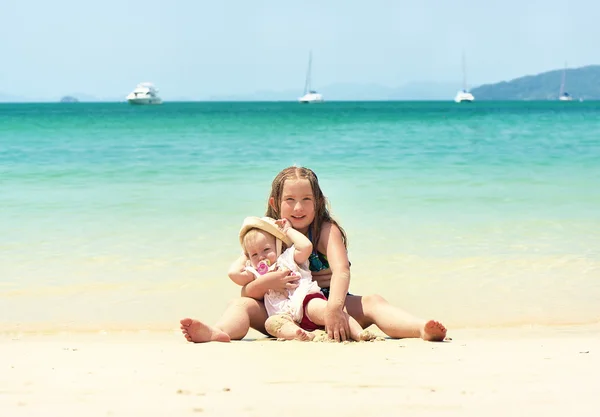 Dos hermanas sonrientes felices sentadas en una playa tropical . — Foto de Stock