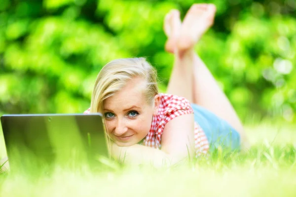Молодая привлекательная женщина лежит на газоне с ноутбуком . — стоковое фото