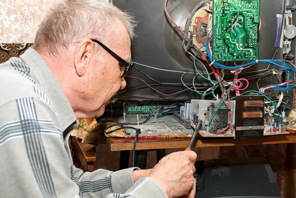 Um homem idoso reparando uma TV antiga — Fotografia de Stock