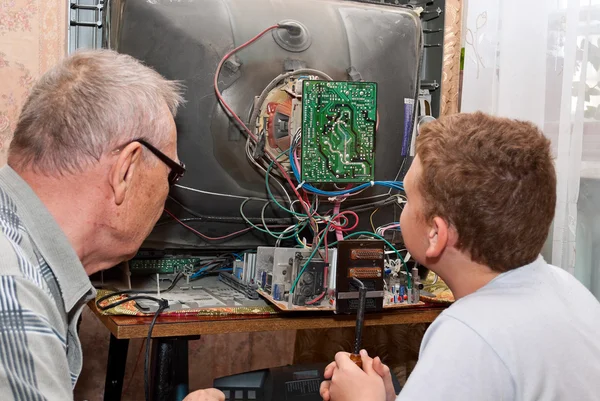 Grandfather and grandson are repairing an old TV