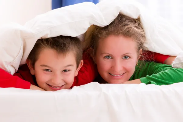 Madre e hijo bajo manta sonriendo alegremente — Foto de Stock