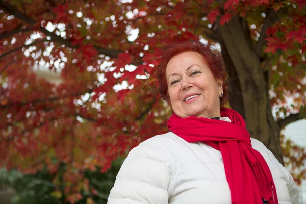 Senhora sênior de cabelo vermelho debaixo da árvore alegremente a olhar para ti — Stok fotoğraf