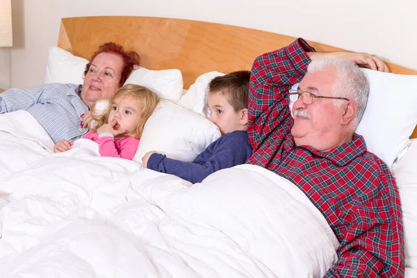 Prarodiče, sledování tv v posteli s dětmi grand — Stock fotografie