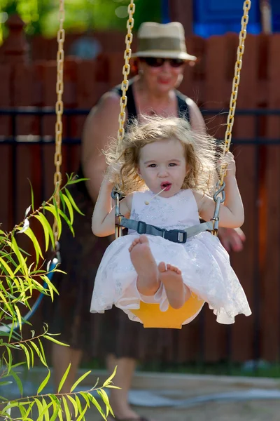 Bambino ragazza su il swing spinto da suo nonna — Foto Stock