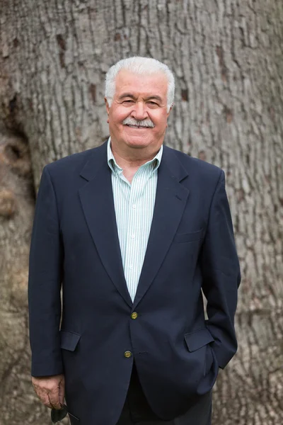 Friendly Senior Adult Looking at You Happily in front of Tree Tr — Stock Photo, Image