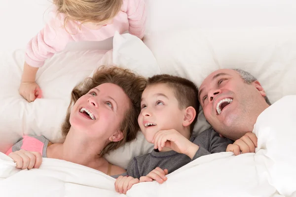 Niña juguetona con su familia en la cama — Foto de Stock