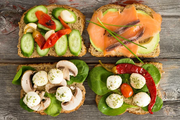 Quatro deliciosos sanduíches abertos em uma mesa de piquenique — Fotografia de Stock