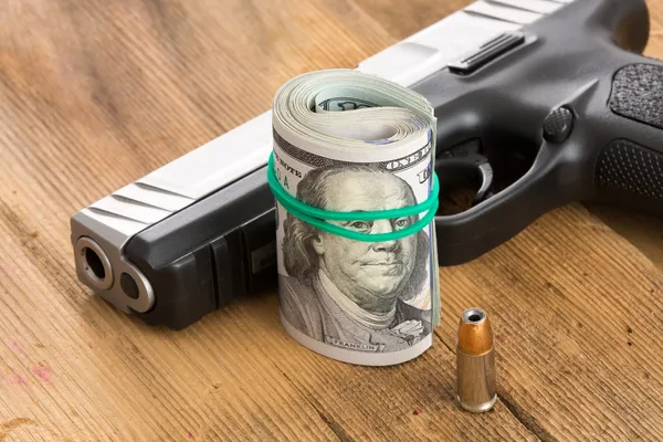 Pistola con un rollo de billetes de dólar y una bala — Foto de Stock