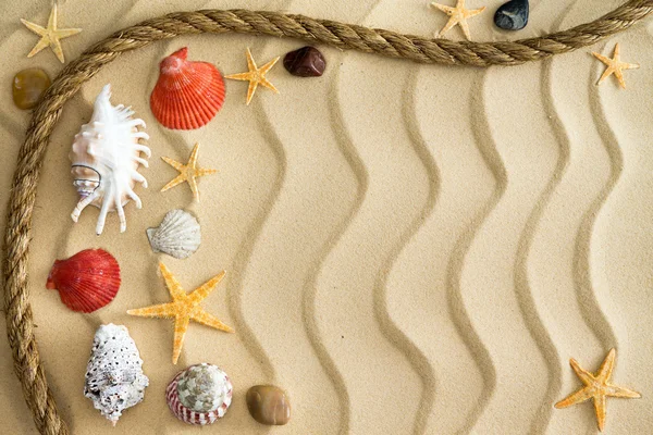 Камушки и ракушки на волнистом песке с веревкой — стоковое фото
