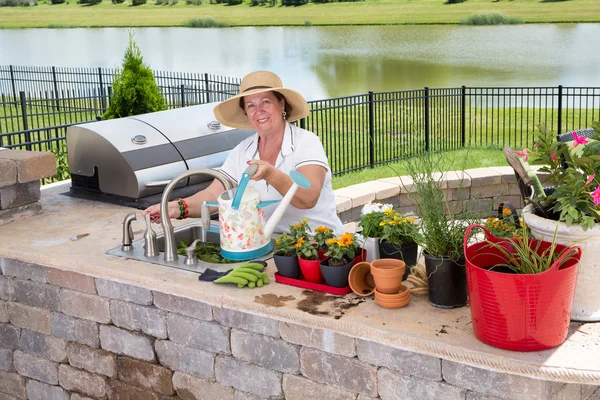 Voormalig senior vrouw tuinieren, in een baksteen patio — Stockfoto