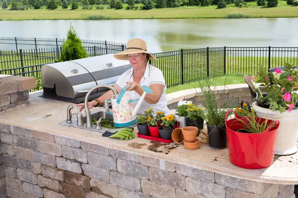 Senior lady filling a watering can on a patio — Stock Photo, Image