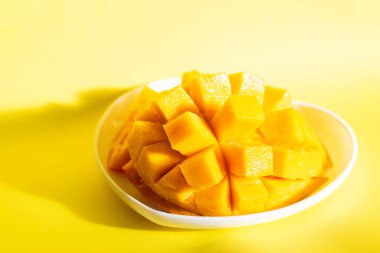 Güzelce dilimlenmiş mango, sarı arka planda bir kalp şeklinde bir tabakta yatıyor. Tropik meyveler.
