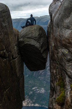 Turist Kjeragbolten 'in tepesinde oturuyor. Kjeragbolten Dağı' nın yarığına sıkışmış kaya parçası. Denizden 984 metre yukarıda.
