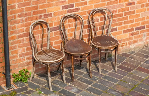 Row of weathered wooden chairs against a brick wall — Stock Photo, Image