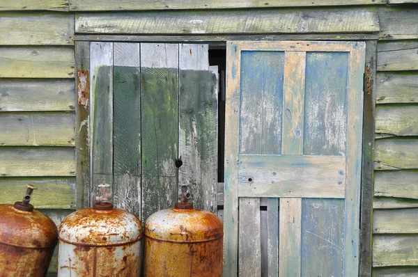 Rusty metal cylinders and weathered shed door — Stock Photo, Image