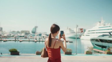 Şirin bir kadın, limanın videolarını cep telefonuyla çekiyor. Kız yat ve gemi vururken sosyal ağları ve akıllı telefondan yayın hizmetlerini kullanıyor.