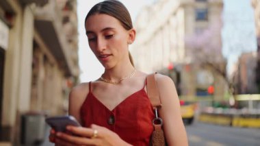 Kapalı çekim gülümseyen genç bayan sokakta cep telefonu kullanıyor. Eski şehrin caddesinde duran kız akıllı telefondaki bilgilere bakıyor..