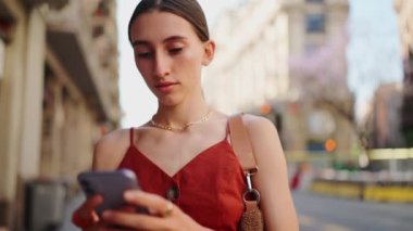 Yakın plan güzel genç bayan şehir arka planında caddenin dışında cep telefonu kullanıyor. Romantik kız şehir merkezine gider ve akıllı telefona bakar..