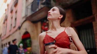 Yakın plan güzel genç bayan sıcak bir şeyler içmek gezmek gibidir. Şehir merkezindeki sokakta güzel kokulu bir kapuçinonun tadını çıkaran kız etrafa dikkatlice bakıyor..