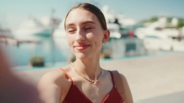 Yakın plan genç bir kadın selfie çekiyor, limanda otururken çekilmiş bir video, cep telefonu kullanıyor. Gülümseyen kız, sosyal medyayı kullan, arka plandaki yat ve gemilerde yayın hizmetini kullan