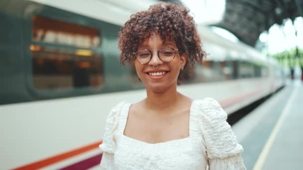 一个戴眼镜的年轻女子的特写站在火车旁边的月台上 微笑着 相机缩放 — 图库视频影像