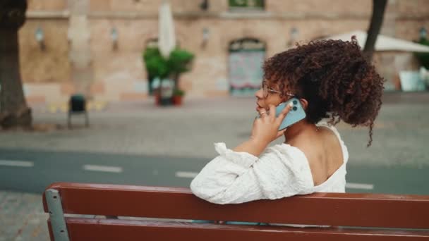 Mujer Joven Gafas Sienta Banco Aire Libre Sonriendo Habla Teléfono — Vídeo de stock