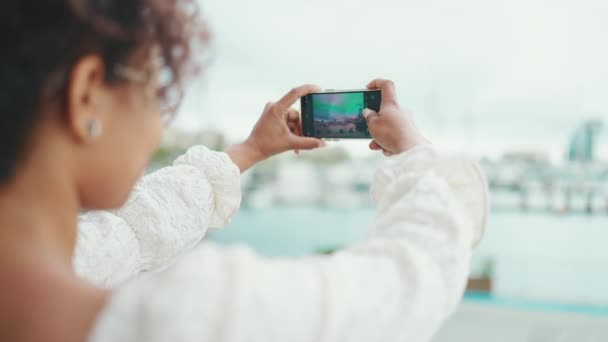 眼鏡をかけた若い女性が港に立ち スマートフォンで船を見て撮影する 都市部の屋外で携帯電話を使用して正の女性 — ストック動画