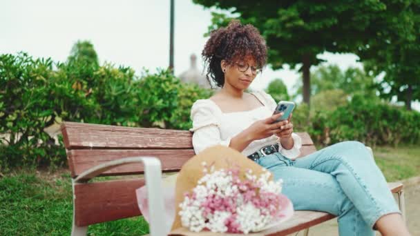 Genç Bir Kadın Elinde Akıllı Telefonuyla Bir Buket Çiçekle Parkta — Stok video