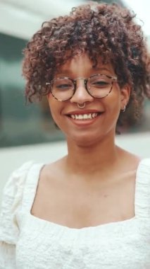 Kameraya bakarken gülümseyen gözlüklü genç bir kadının yakın plan portresi. Mutlu bir kızın portresi. Kamera yakınlaştırılıyor