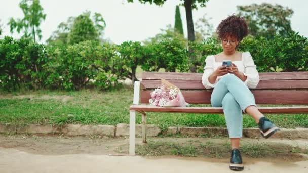 Jovem Mulher Senta Parque Banco Com Buquê Flores Com Smartphone — Vídeo de Stock