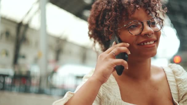 一个戴眼镜的年轻女子坐在车站 用智能手机聊天的特写镜头 城市背景下在室外使用手机的阳性妇女 — 图库视频影像